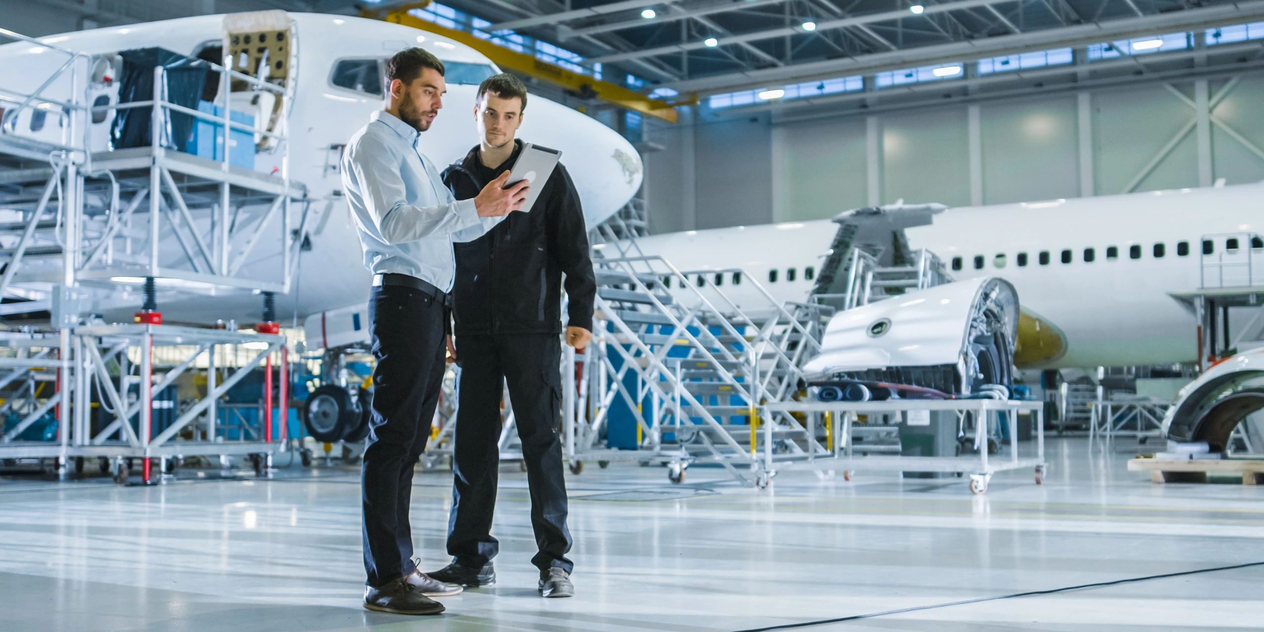 Aircraft Maintenance Worker and Engineer having Conversation. Holding Tablet.