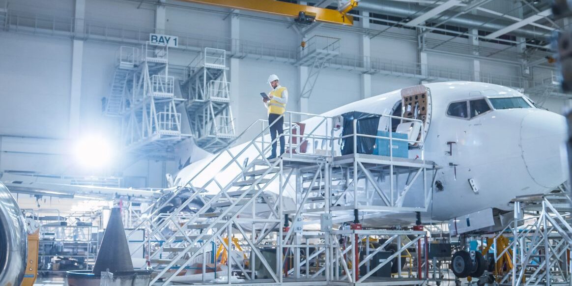Engineer in Safety Vest Standing next to Airplane in Hangar
